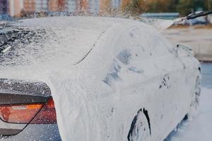 coche en espuma de jabón blanco durante la limpieza con lavadora de alta presión en la estación de lavado de coches foto