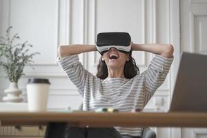 Amazed woman office employee in VR glasses laughing and leaning back in chair with hands behind head