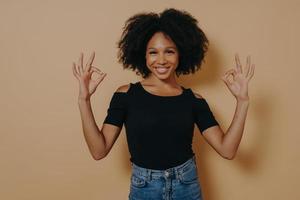 Young african female shows ok sign okay gesture with both hands, isolated over beige background photo