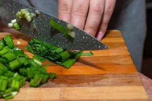 primer plano de manos sosteniendo cebollas verdes en una tabla de cortar de madera. cocinar verduras en la cocina. foto