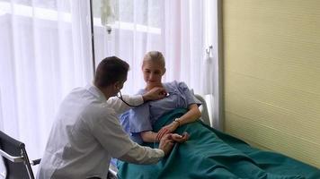 médico masculino que usa estetoscopio en una paciente en la cama en la sala de examen de la clínica video