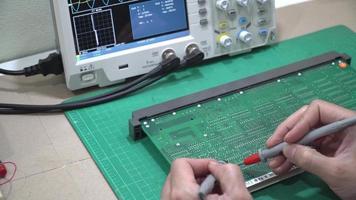 le technicien inspecte la carte de circuit imprimé par un oscilloscope à stockage numérique. video