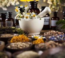 Assorted natural medical herbs and mortar on wooden table background photo