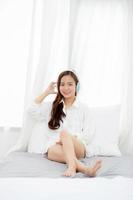 Beautiful asian young woman enjoy listen music with headphone while sitting in bedroom, relax girl with earphone internet online, leisure and technology concept. photo