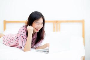 Beautiful of portrait asian young woman lying relax and leisure with laptop internet online on vacation in bedroom, cheerful of asia girl with gesture glad and success, lifestyle concept. photo