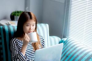 Beautiful of portrait young asian woman sitting use credit card with laptop and drink coffee, Content girl shopping online and payment with notebook computer on sofa, lifestyle concept. photo