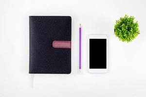 Black cover leather notebook or diary for reminder and memo isolated on white background, book mockup pencil tree and smart phone on desk office, education and supplies concept, top view. photo