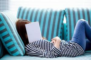 hermosa joven asiática durmiendo en un sofá con un libro cubriendo su rostro porque lee un libro con la preparación del examen de la universidad, una chica somnolienta con cansancio para que el concepto de ocio, relajación y educación. foto