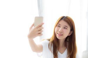 hermoso retrato joven asiática tomando un selfie con un teléfono móvil inteligente en el dormitorio por la mañana en casa, la chica está fotografiando con felicidad y sonrisa con un concepto de estilo de vida divertido. foto