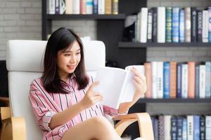 hermosa de retrato joven mujer asiática relajarse sentado leyendo un libro en la sala de estar en casa, niña estudiar literatura, educación y concepto de estilo de vida. foto