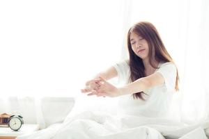 Beautiful young asian woman stretch and relax in bed after wake up morning at bedroom, back view, new day and resting for wellness, lifestyle concept. photo