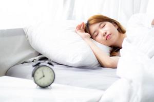 closeup alarm clock and beautiful asian young woman in morning, wake up for sleep with alarm clock, relax and lifestyle concept. photo