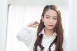 hermosa de retrato mujer joven asiática examinando con cara y sonrisa mirando en el espejo en el dormitorio, chica belleza de maquillaje y vestida con reflexión, estilo de vida y concepto de bienestar. foto