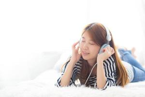 hermosa mujer joven asiática disfruta y se divierte escuchando música con auriculares en el dormitorio, la chica se relaja con el concepto de auriculares, ocio y tecnología. foto
