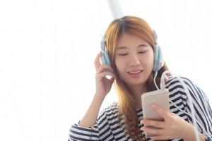 hermosa joven asiática disfruta escuchando música con auriculares y sosteniendo un teléfono móvil inteligente mientras está sentada en el dormitorio, relaja a la chica con el concepto de auriculares, ocio y tecnología. foto