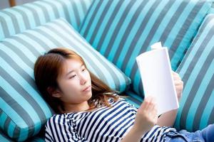 hermosa de retrato joven mujer asiática relajarse acostado leyendo un libro en el sofá en el dormitorio en casa, niña estudia literatura, educación y concepto de estilo de vida.