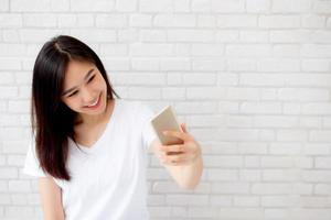 Beautiful portrait young asian woman taking a selfie with smart mobile phone on concrete cement white background, girl is photographing with happy and smile with fun, lifestyle concept. photo