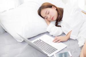 Beautiful young asian woman with laptop lying down in bedroom, girl tired sleep with computer notebook and smart mobile phone, resting and healthcare concept.