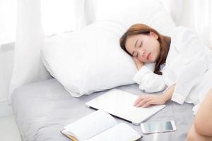 Beautiful young asian woman with laptop lying down in bedroom, girl tired sleep with computer notebook and smart mobile phone, resting and healthcare concept. photo