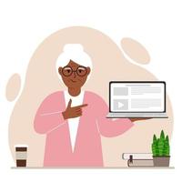 Happy grandmother holding a laptop computer with one hand and pointing at it with the other. Laptop computer technology concept. Vector flat illustration
