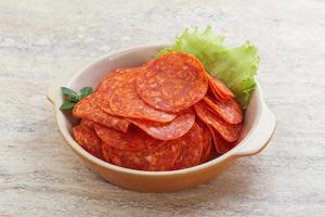 Sliced pepperoni sausage in the bowl photo