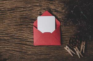 una tarjeta en blanco con un sobre rojo y una pinza para la ropa colocada en el fondo de madera foto