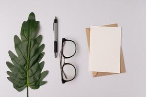 sobre, tarjeta, bolígrafo, cuaderno, gafas y ramas de hojas sobre fondo blanco foto