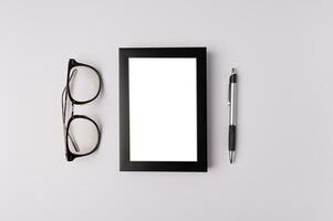 black photo frame, glasses and pen on white background