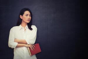 hermosa mujer sosteniendo un libro y mira la pizarra foto