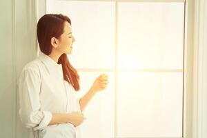 Beautiful young woman looking out in window at home and smiley so happy photo