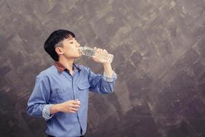 Handsome young asian man drinking water in front of grunge background photo