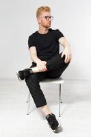 Young man on a chair, Portrait of handsome young man sitting on a chair, Proud and satisfied young man sitting on chair and looking at camera isolated, Casual young man in glasses photo