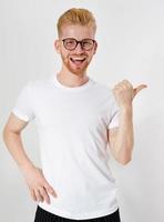 Stylish red-haired smile man in a white T-shirt points a finger to the side photo