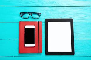 Electronic devices with places for text. Notebook and glasses. Blue wooden background and top view photo