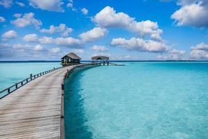 paisaje panorámico de la playa de maldivas. panorama tropical, complejo de lujosas villas acuáticas con muelle de madera o embarcadero. fondo de destino de viaje de lujo para vacaciones de verano y concepto de vacaciones. foto