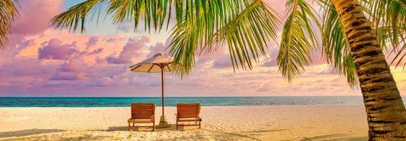 Summer beach landscape. Luxury vacation and holiday concept, summer travel banner. Panoramic landscape of sunset beach, two loungers umbrella, palm leaf, colorful sunset sky for paradise island view photo