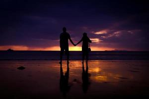 silueta de pareja tomándose de la mano y feliz pareja joven amor en la playa al atardecer foto