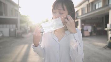 edad de la mujer trabajadora asiática con mascarilla protectora, protegerse del coronavirus covid19, parada en el lado de la calle, puesta de sol dorada al aire libre, parada alrededor del vecindario, distanciamiento social