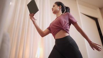 A female sportive young adult stretching after relaxing exercise, does meditation, student holding lecture book for reading while doing yoga at home living room, people and hobbies, preparing for exam video