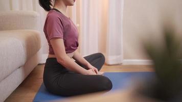 Asiatisk ung som mediterar på blå yogamatta hemma i vardagsrummet, hemmeditation under covid-19-låsning, håll dig lugn och slappna av, hälsosam livsstil för mänskligt välbefinnande, flexibel kropp med yoga. själv motivation video