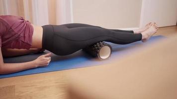 joven mujer asiática en forma y firme masajeando los músculos de sus piernas usando espuma rodando sobre yoga matt dentro de la sala de estar el fin de semana, atención médica y tratamiento alternativo, rehabilitación en medicina deportiva video