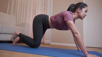 chica asiática en forma haciendo ejercicio en la sala de estar de casa. entrenamiento de glúteos, entrenamiento en casa en colchoneta de ejercicios, entrenamiento de condición corporal y bienestar pasando tiempo activo en casa. estilo de vida saludable video