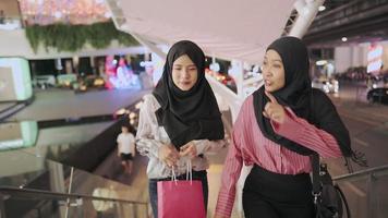 zwei asiatische muslimische frauen, die die treppe im einkaufszentrum hinaufgehen, mädchen, die zeit miteinander verbringen, schaufensterbummel kunden mitglied konsumismus kaufen produkte, einkaufstasche halten, markenverkäufe