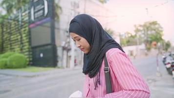 attraente fatica asiatica musulmana femmina con hijab nero passeggiando su un ciglio della strada con le mani in possesso di una tazza di carta da caffè da asporto, una notte insonne, giovane lavoratore adulto che cammina verso l'ufficio nella zona degli affari video