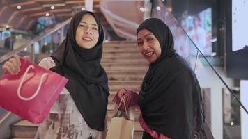 zwei junge asiatische muslimische frauen fühlen sich glücklich, einkaufstaschen vor der kamera zu zeigen, modernen muslimischen lebensstil, wochenendaktivitäten, geld auszugeben, rabatte verkaufsprodukte, genießen sie das einkaufen im einkaufszentrum, das stadtleben video