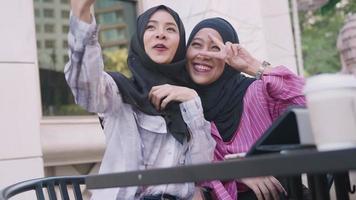 jeunes femmes musulmanes asiatiques joyeuses en hijab prenant des selfies dans leur ambiance de l'après-midi, s'asseoir dehors au café, amitié musulmane moderne, capturer des souvenirs, profiter de voyager avec des amis