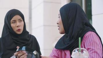 duas jovens muçulmanas usam hijab no intervalo do café da tarde, conversando com garotas, sentam-se descansando no café, socializam a cultura islâmica, amizade desfrutam do bom tempo lá fora video