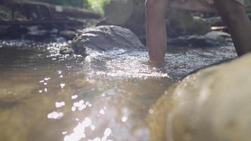 eine hellhäutige weibliche Beine, die tagsüber durch den fließenden Fluss im Nationalpark laufen, ein wunderschöner natürlicher Wasserstrom mit Sonne, die sich auf der Oberfläche widerspiegelt, erfrischende Aktivität, die die Natur berührt