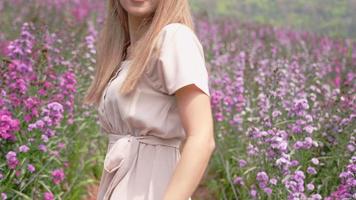una feliz y elegante chica rubia asiática bailando a cámara lenta al aire libre dentro de un campo de flores púrpura, una joven atractiva que se siente libre dando vueltas en el jardín de primavera en el día de verano, tocando la naturaleza video