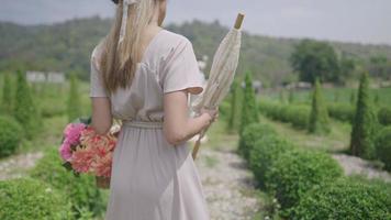 Rear view of young elegance beautiful girl walks through a vintage Europe decor style garden, natural summer sunlight shines as a background, enjoying holiday travel vacation adventure, POV follower video